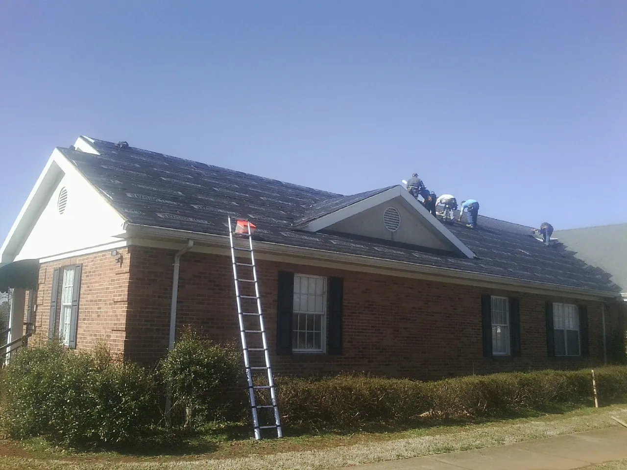 Crew tearing shingles off a brick ranch roof with a ladder set — Metal Roof Repair work by our crew in Louisville